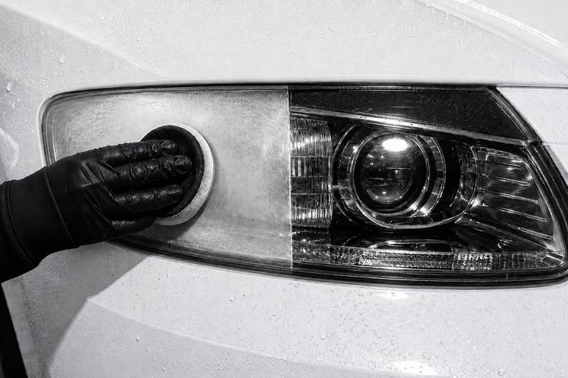 Gloved hand polishing a cloudy headlight lens, with the restored half of the lens shown clear